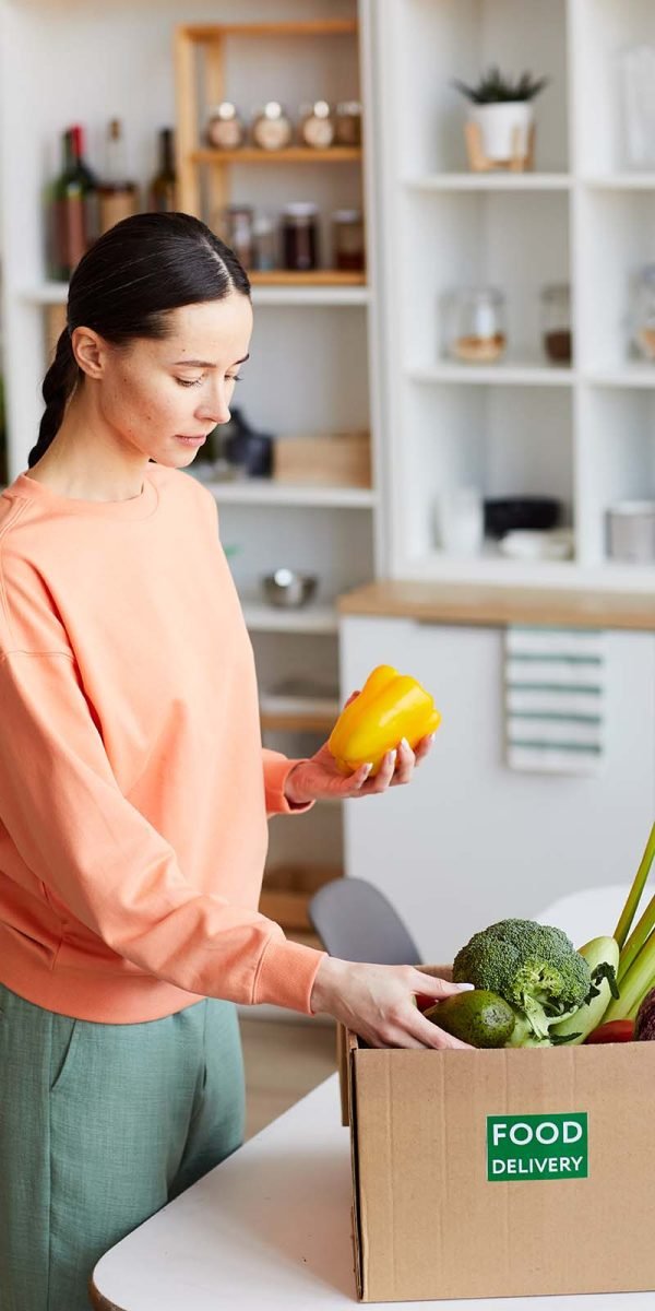 Young woman getting the box with fresh vegetables she standing in the kitchen and unpacking it